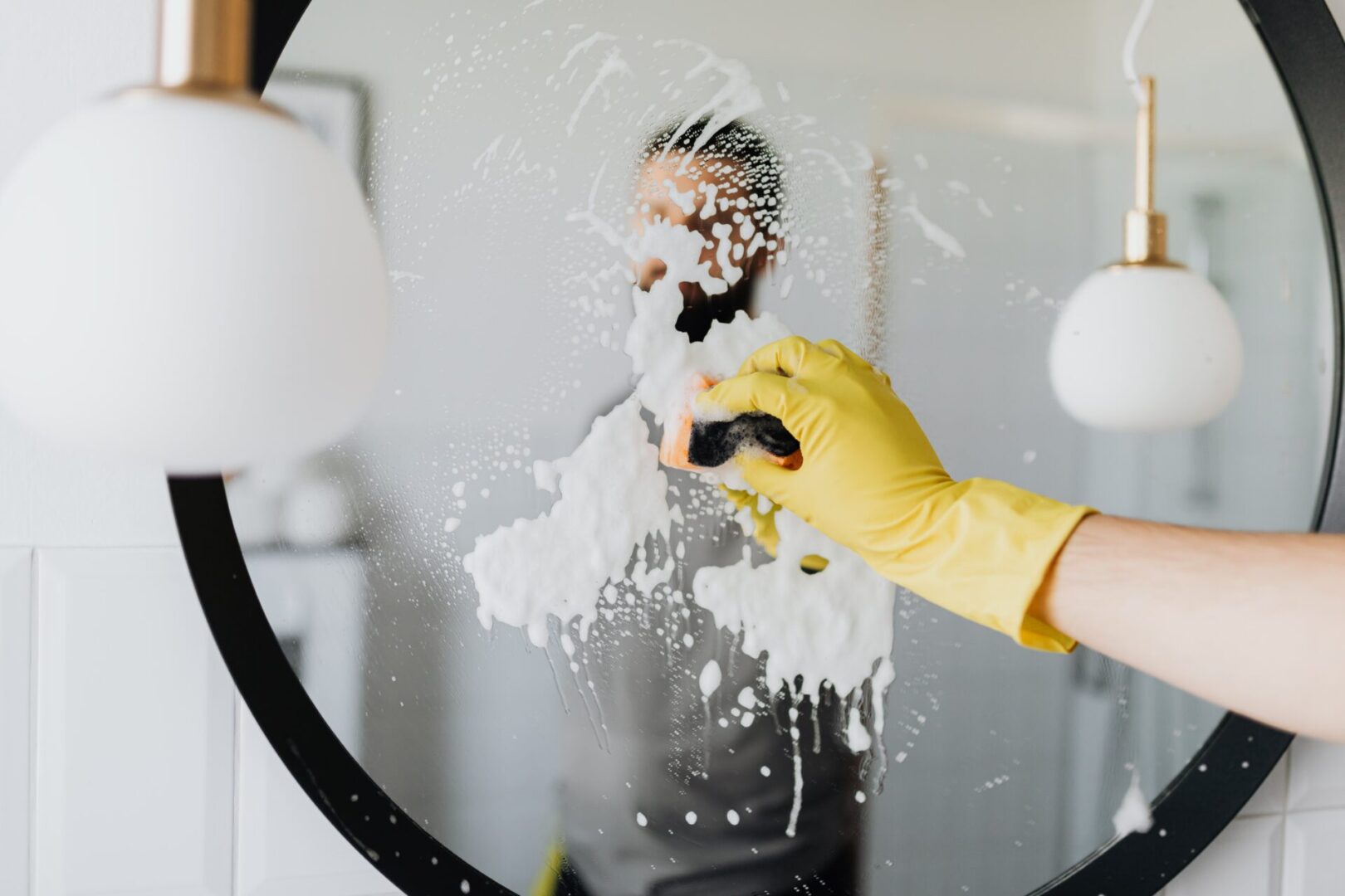 A person with yellow gloves is cleaning the mirror