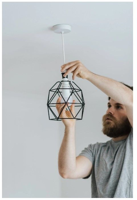 A man is hanging a cage light fixture.