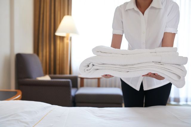 A person holding folded white towels in front of a bed.